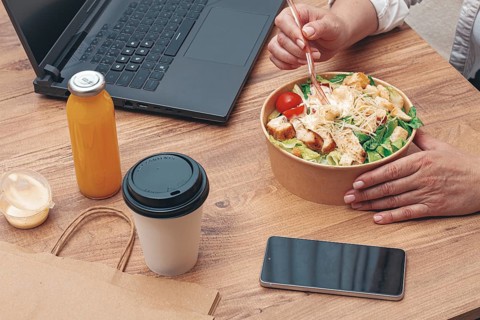 A woman is working on a laptop at home, there is food on the table, salad, coffee and juice,