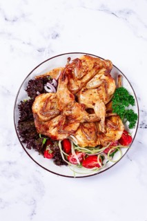Baked quail, served on a plate with crispy lettuce leaves, fresh tomatoes and herbs, on a white