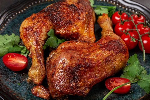 Grilled fried chicken legs, served with fresh cherry tomatoes and herbs, on a plate, homemade, no