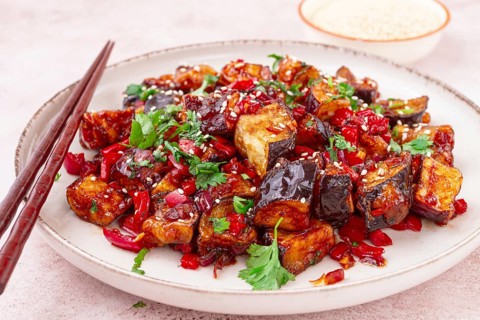 Fried eggplant, Chinese style, in sweet and sour sauce, with pepper and sesame seeds. on a white