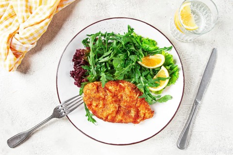Milanese chicken, Crispy breaded chicken served, with fresh herbs, and lemon wedges