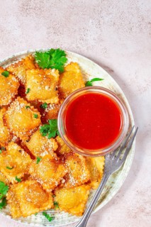 Fried ravioli with parmesan cheese, served with red sauce and garnished with herbs, on a light