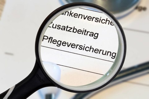 (Photomontage) Close-up of the word PFLEGEVERSICHERUNG on a document, enlarged with a magnifying