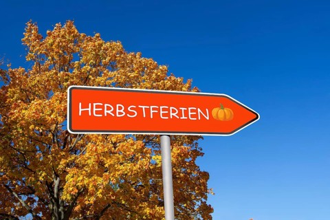 (Photomontage) Directional arrow with the inscription HERBSTFERIEN in front of an autumn-coloured