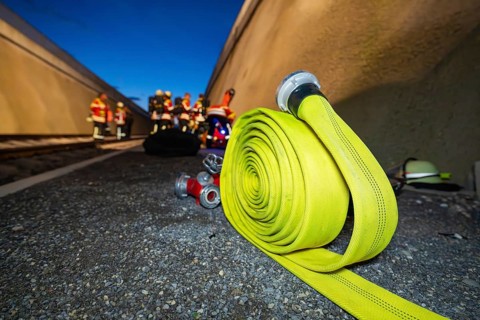 A yellow fire hose lies on the ground, with firefighters in the background, fire drill in the new