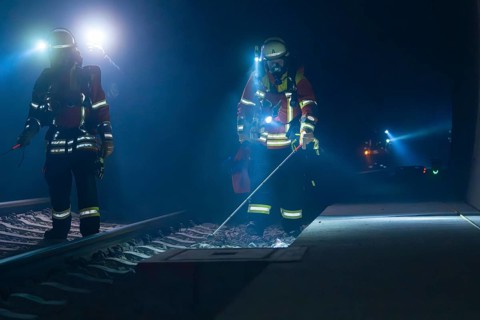 Firefighters working on railway tracks at night with torches and safety equipment, firefighting