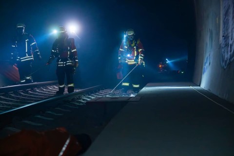 Three firefighters walking along a tunnel wall, torch lit, fire drill in the new tunnel of the