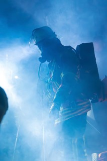Firefighter in smoke with breathing apparatus and helmet, blue light surrounding him, fire drill in