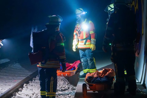 Group of firefighters at night on railway tracks with rescue stretchers, firefighting exercise in