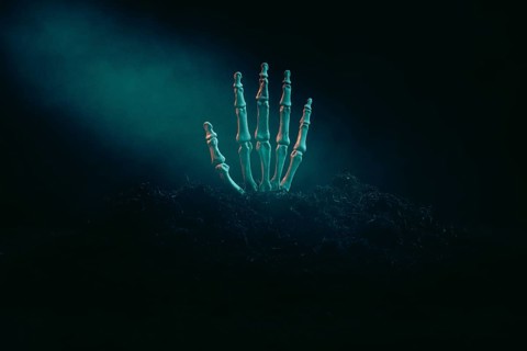A skeleton hand protruding from the dark earth in the dim light, Halloween
