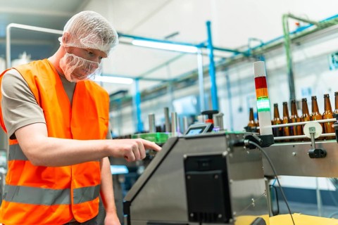 Male worker in protective gear overseeing automated beer bottling and labeling on a clean modern