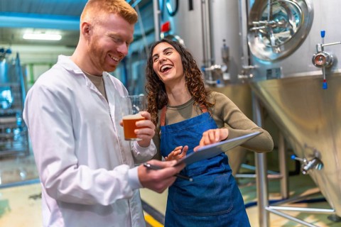 Man and woman tasting and checking craft beer quality, smiling and laughing together while