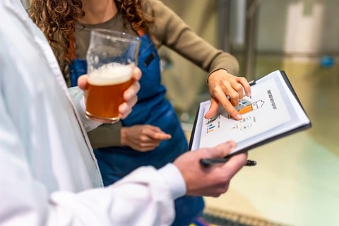 Brewery staff discussing quality control data and production metrics from a clipboard report while