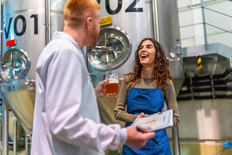 Brewery worker and quality control specialist smiling, holding clipboard and a glass of beer,