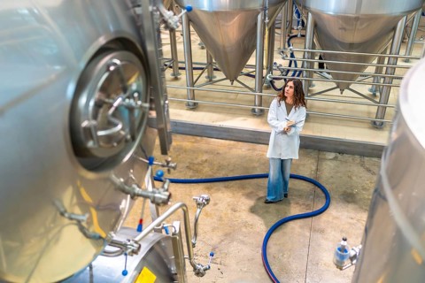 Female scientist wearing a lab coat and holding a clipboard, observing stainless steel fermentation