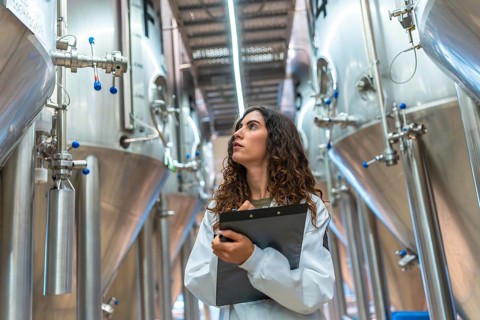 Woman in laboratory coat conducting quality control inspection in a modern beer brewery, holding a