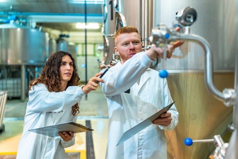 Chemical engineers and a quality control technician are checking stainless steel fermentation tanks
