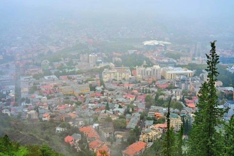 View of a city blanketed in fog with buildings and greenery in the foreground. Various buildings