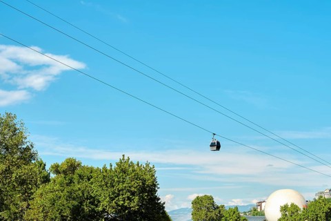 A cable car travels smoothly across a bright sky, suspended over a rich canopy of trees