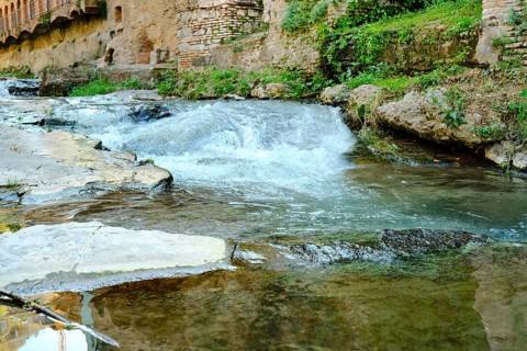 Gentle water flows over smooth stones revealing a tranquil scene. Surrounded by ancient walls and