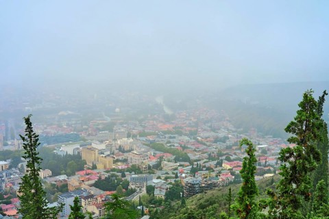 A dense fog blankets the city of Tbilisi, obscuring buildings and creating a mystical atmosphere