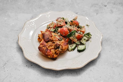 A hearty baked dish sits on a decorative plate alongside a vibrant vegetable salad. The salad