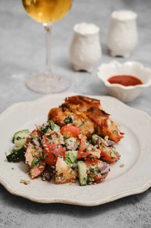 A fresh salad made with tomatoes, cucumbers, and herbs is served alongside grilled chicken