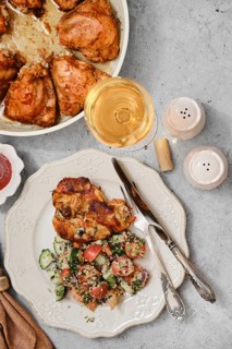 Grilled chicken pieces are plated next to a vibrant salad made of cucumbers and tomatoes. A glass