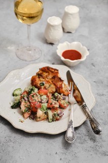 A well-prepared meal features grilled chicken, fresh salad with tomatoes and cucumbers, and a glass