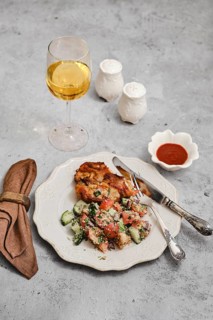 A beautifully arranged meal includes a golden glass of wine, a serving of baked meat, fresh salad
