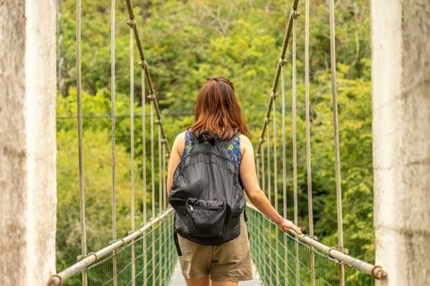 Female tourist with backpack walking on a hanging bridge over the sella river, surrounded by lush