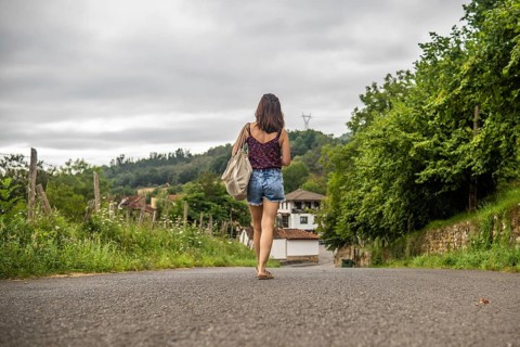 Young woman tourist walking on a road approaching benia de onis village in asturias, spain, during