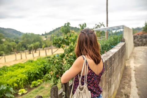 Young woman tourist with backpack is enjoying the view of a peach orchard and a vegetable garden in