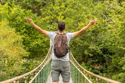 Backpacker opening his arms while enjoying the view from a hanging bridge over the sella river,