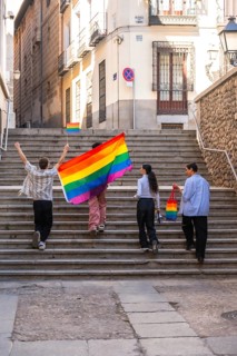 Group of diverse friends celebrating pride, walking up old stairs in a city, carrying a large