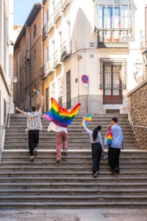 Young adults are joyfully walking up stone stairs in a european city, carrying rainbow flags and a