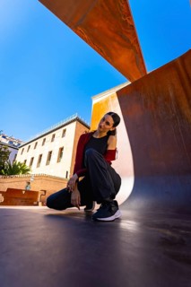 Young woman posing in a modern city environment, featuring rust colored metal structures and
