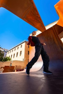 Woman performing a dynamic dance move, expressing freedom and urban culture against a vibrant blue