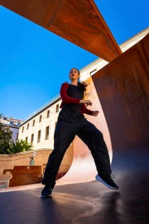 Young woman moving energetically, practicing dance in an urban setting, with modern corten steel