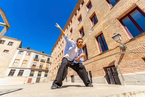 Young man actively posing or dancing in a dynamic stance on a sunny urban street, expressing