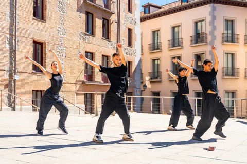 Group of diverse urban dancers performing synchronized street dance movements with raised arms and