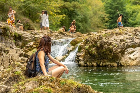 Young female hiker resting on rocks near a small waterfall on the dobra river, with other hikers