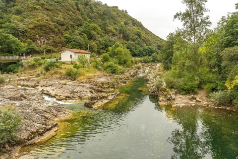 Sella river meandering through a rocky riverbed, surrounded by lush vegetation, trees, and a small