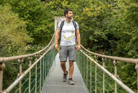 Male hiker with backpack enjoying trekking in the forest, walking on a metallic hanging bridge over