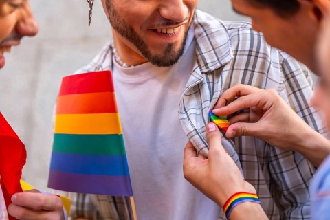 Happy man smiles as someone pins a rainbow flag badge to his plaid shirt, celebrating lgbtq pride,