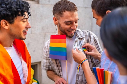 Group of young people smiling and interacting at a pride event, one person receiving a rainbow pin