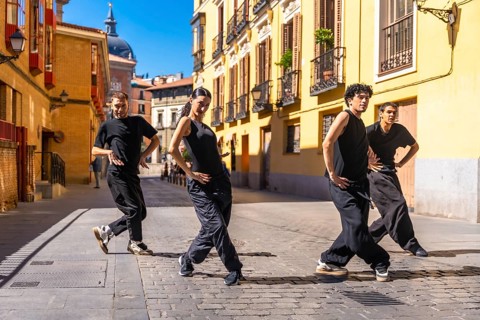 Group of urban dancers in black clothes performing a contemporary dance routine on a cobbled street