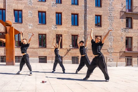 Four young male and female dancers performing a synchronized urban choreography with arms raised,