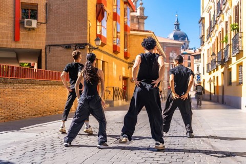 Group of young people standing in an urban cobblestone street, performing an energetic street dance