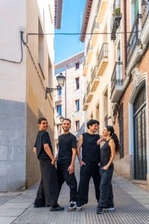 Group of diverse dancers wearing black casual clothing are posing and smiling while looking at the